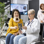 Doctor examining woman patient with neck fracture during routine appointment in modern clinic lobby. Medic offers includes recommendations for physiotherapy and appropriate painkillers.