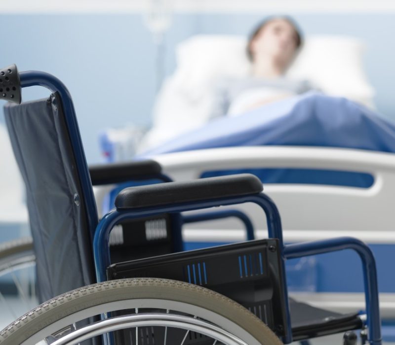 Hospitalized patient lying in bed and wheelchair in the foreground, medical treatment and injury concept